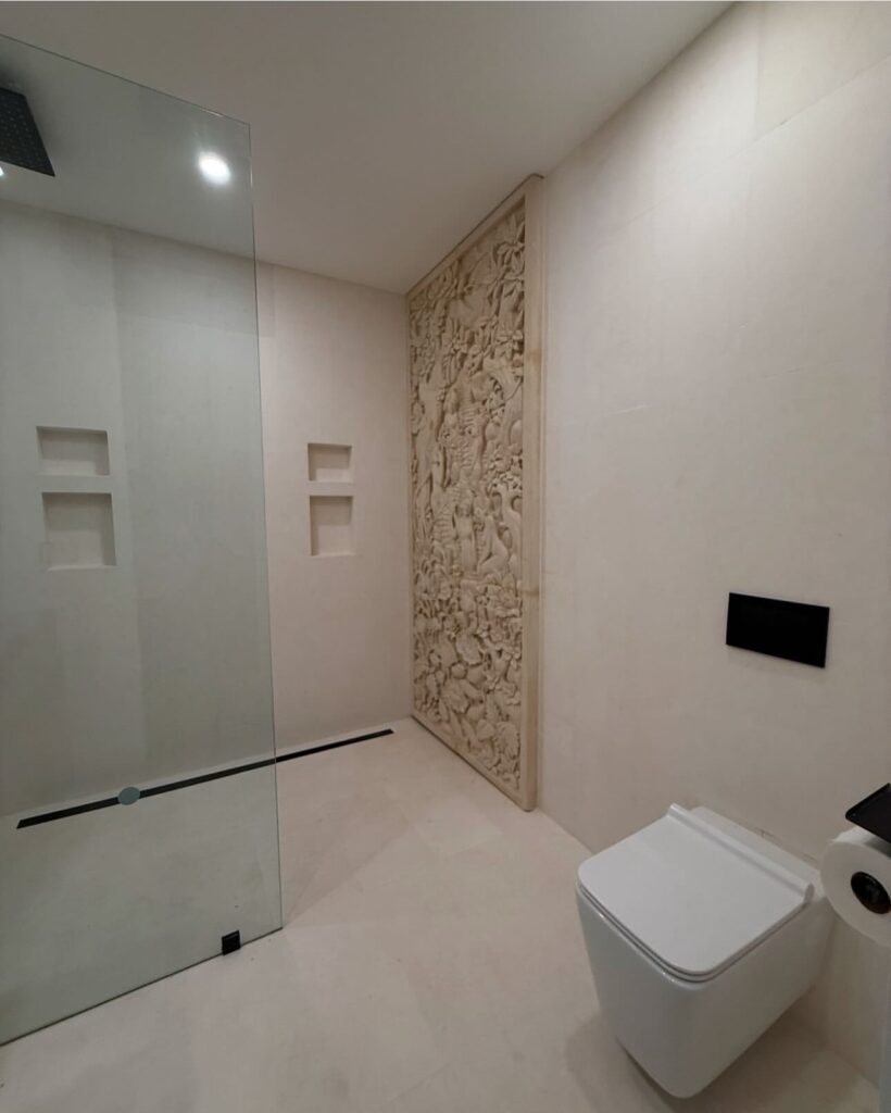 Wet room with carved stone feature wall and linear drain